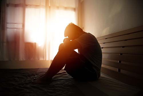 a person sitting on the ground with their head by their knees thinking about depression and substance use