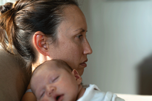 A woman struggles with depression while holding her baby. She is in need of postpartum depression treatment.